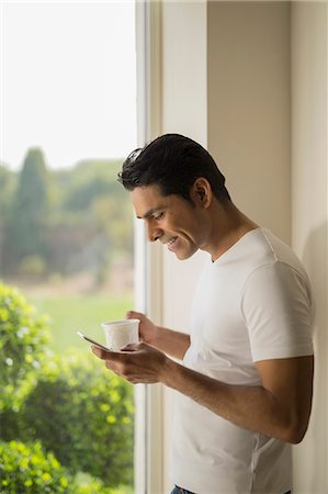 simsearch:655-08357057,k - India, Man at window holding coffee cup and mobile phone Photographie de stock - Premium Libres de Droits, Code: 655-08356963