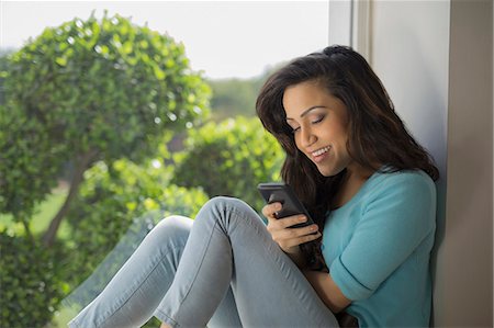 simsearch:655-08357057,k - India, Woman sitting at window looking down at mobile phone Photographie de stock - Premium Libres de Droits, Code: 655-08356976