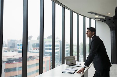 simsearch:655-08357080,k - India, Businessman standing by desk and looking through window in office Stock Photo - Premium Royalty-Free, Code: 655-08357107