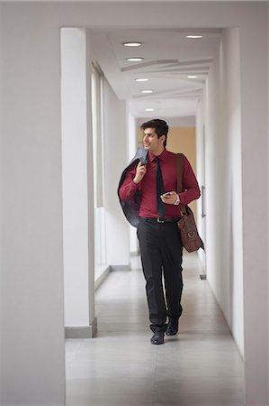simsearch:655-08357168,k - India, Man walking down corridor with jacket over shoulder and phone in hand Photographie de stock - Premium Libres de Droits, Code: 655-08357167
