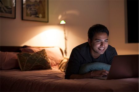 pictures candid bedroom - Singapore, Young man relaxing with laptop on bed Stock Photo - Premium Royalty-Free, Code: 655-08357179