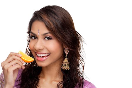 simsearch:655-01781410,k - A young woman smiles at the camera as she eats a slice of orange Fotografie stock - Premium Royalty-Free, Codice: 655-01781422