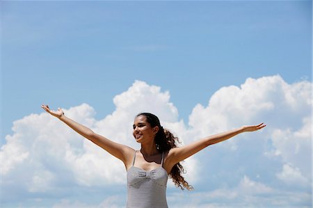 young woman lifting up her arms with blue sky and clouds background Stock Photo - Premium Royalty-Free, Code: 655-03519589