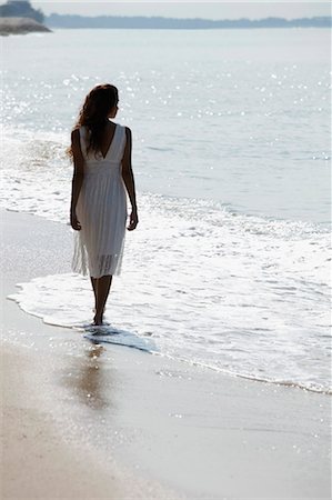 back view of woman wearing white dress and walking along the beach Stock Photo - Premium Royalty-Free, Code: 655-03519654