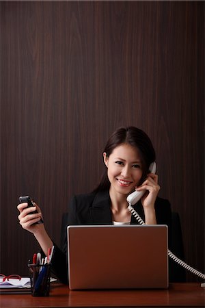 simsearch:656-04926491,k - Young woman sitting at her desk holding her phones Stock Photo - Premium Royalty-Free, Code: 656-04926468