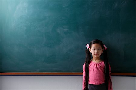 Young girl with pony tails standing in front of chalkboard Stock Photo - Premium Royalty-Free, Code: 656-04926584