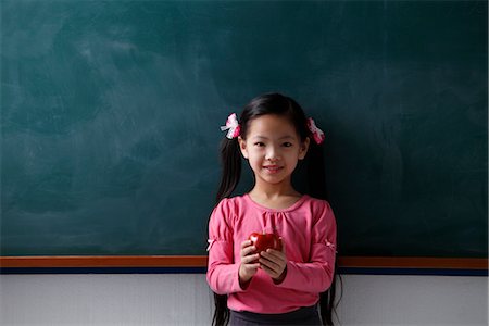 simsearch:614-05523144,k - Young girl holding a red apple in front of chalk board Stock Photo - Premium Royalty-Free, Code: 656-04926587