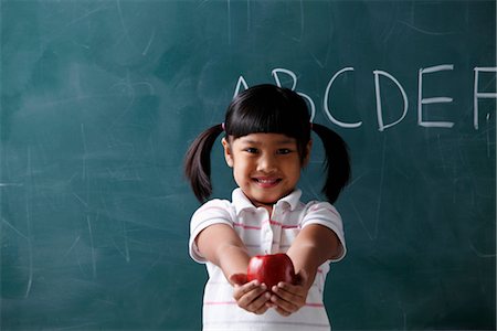 young girl holding out apple in front of chalkboard Stock Photo - Premium Royalty-Free, Code: 656-04926618