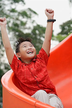 energized - Boy coming down playground slide, arms outstretched, smiling, looking up Stock Photo - Premium Royalty-Free, Code: 656-01765200