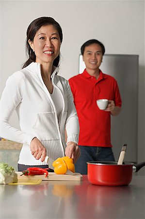 Mature woman in kitchen preparing a meal, man standing behind her, both looking at camera Stock Photo - Premium Royalty-Free, Code: 656-01765213