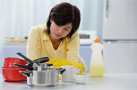 simsearch:656-01765881,k - Woman in kitchen, leaning on kitchen counter, looking at stack of pots and pans Foto de stock - Royalty Free Premium, Número: 656-01765341