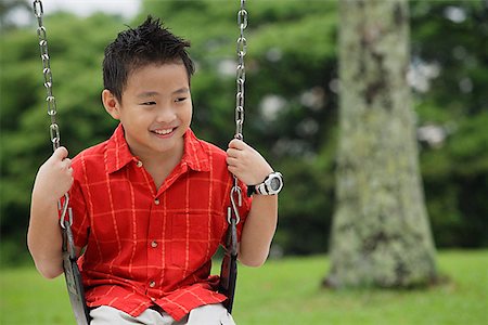 Boy in red shirt sitting on swing smiling Stock Photo - Premium Royalty-Free, Code: 656-01765360