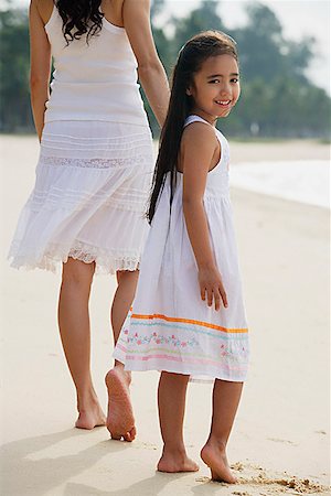 simsearch:656-01765470,k - Mother and daughter walking down beach, daughter looking back towards camera smiling Foto de stock - Sin royalties Premium, Código: 656-01765410