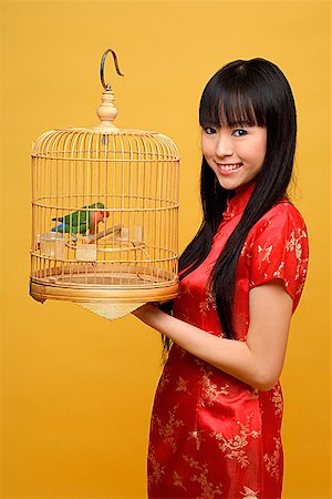 fashion red dress studio shot - Young woman holding lovebird in bird cage, smiling Stock Photo - Premium Royalty-Free, Code: 656-01765436