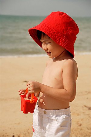 simsearch:841-03507749,k - Young boy on beach, wearing red hat and carrying red beach bucket Stock Photo - Premium Royalty-Free, Code: 656-01765445