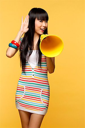 simsearch:656-01765511,k - Young woman talking through yellow megaphone, hand to ear Stock Photo - Premium Royalty-Free, Code: 656-01765484