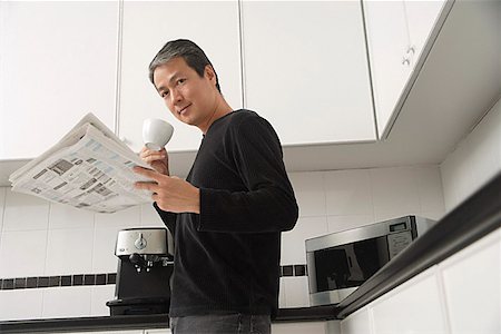 Man in kitchen, holding coffee cup and newspaper and looking at camera Stock Photo - Premium Royalty-Free, Code: 656-01765532