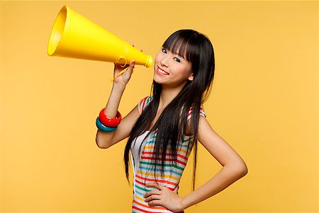 Young woman holding yellow megaphone and smiling at camera Stock Photo - Premium Royalty-Free, Code: 656-01765542