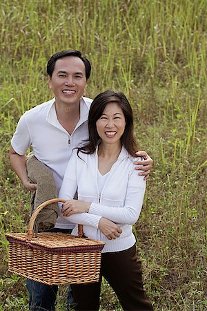 simsearch:656-01765785,k - Man and woman standing outdoors in nature, holding picnic basket, smiling at camera Stock Photo - Premium Royalty-Free, Code: 656-01765619