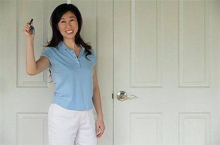 door house key - Woman standing next to door, holding house keys, smiling Stock Photo - Premium Royalty-Free, Code: 656-01765807