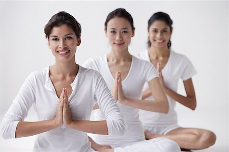 three women of mixed race sitting with legs crossed, arms in namaste, smiling at camera Stock Photo - Premium Royalty-Free, Code: 656-01765876