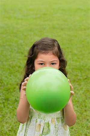 Girl standing on grass, holding green balloon over her face Stock Photo - Premium Royalty-Free, Code: 656-01765873