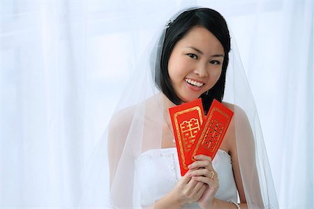 A bride smiles at the camera and holds out two red envelopes Stock Photo - Premium Royalty-Free, Code: 656-01765975
