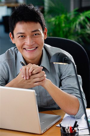 simsearch:656-01766255,k - A man smiles at the camera as he sits at his desk Stock Photo - Premium Royalty-Free, Code: 656-01766156