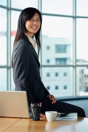 simsearch:656-01766255,k - A woman smiles at the camera as she sits on her desk Stock Photo - Premium Royalty-Free, Code: 656-01766303