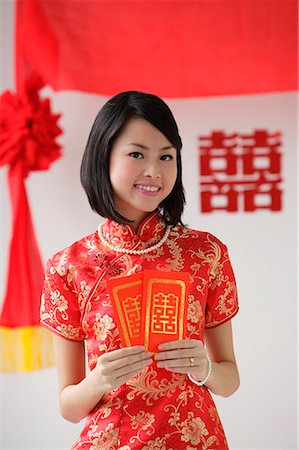 A bride smiles as she holds two red envelopes Stock Photo - Premium Royalty-Free, Code: 656-01766454