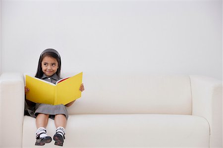 studying sofa - A young girl dressed in school uniform sitting down with a book Stock Photo - Premium Royalty-Free, Code: 656-01766466