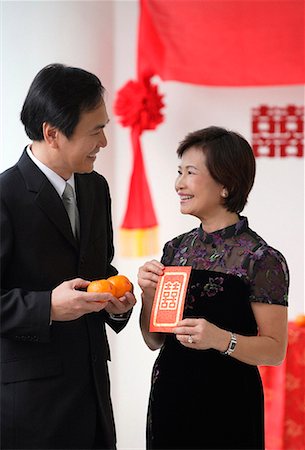 simsearch:656-01766432,k - A couple smile as they hold two oranges and a red envelope Foto de stock - Sin royalties Premium, Código: 656-01766559