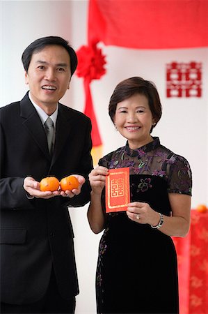 simsearch:656-01766432,k - A couple look at the camera as they hold two oranges and a red envelope Foto de stock - Sin royalties Premium, Código: 656-01766599