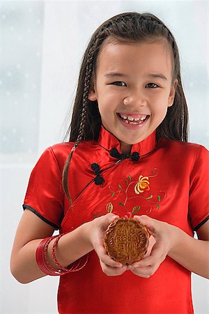 Young girl in traditional Chinese dress holding cookie and smiling at camera Stock Photo - Premium Royalty-Free, Code: 656-01766635