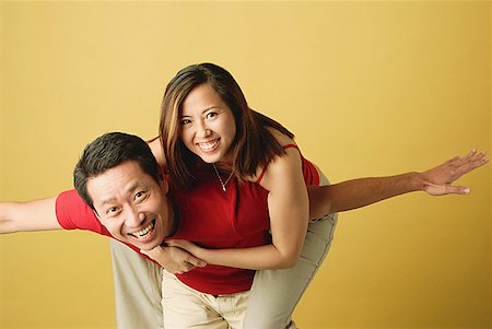 singapore women 30s - Man carrying woman on back, arms outstretched Stock Photo - Premium Royalty-Free, Code: 656-01767414