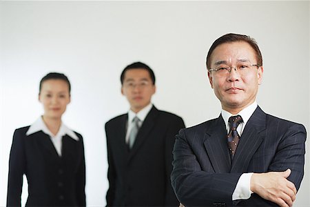 simsearch:656-01767698,k - Businessman with arms crossed, looking at camera, two executives behind him Foto de stock - Royalty Free Premium, Número: 656-01767644