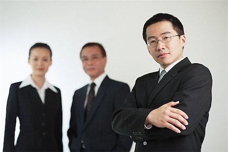 simsearch:628-02954142,k - Young businessman with arms crossed, businessman and businesswoman in the background Fotografie stock - Premium Royalty-Free, Codice: 656-01767645