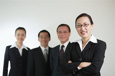 Businesswoman with arms crossed, other executives in the background, smiling Stock Photo - Premium Royalty-Free, Code: 656-01767647