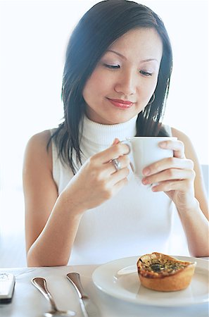 singapore women 30s - Young woman, holding coffee cup, food on plate in front of her Stock Photo - Premium Royalty-Free, Code: 656-01767800