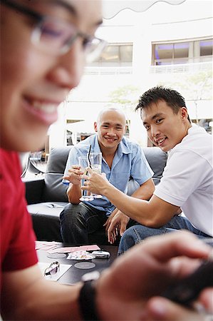 simsearch:656-03519571,k - Two men toasting with drinks, looking at camera, another man using mobile phone in the foreground Foto de stock - Sin royalties Premium, Código: 656-01767886