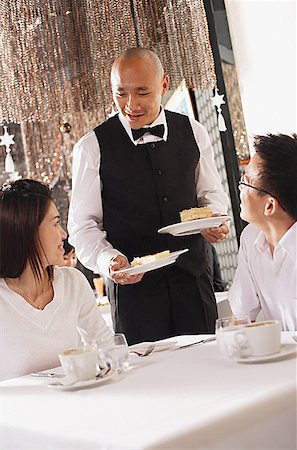 singapore women 30s - Couple in restaurant, waiter standing next to their table, holding plates of dessert Stock Photo - Premium Royalty-Free, Code: 656-01767903