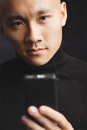 Man with shaved head, holding mobile phone, looking at camera selective focus Stock Photo - Premium Royalty-Free, Code: 656-01768038