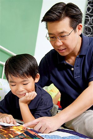 simsearch:656-01768333,k - Boy lying on bed, reading a book, father next to him pointing at book Stock Photo - Premium Royalty-Free, Code: 656-01768206