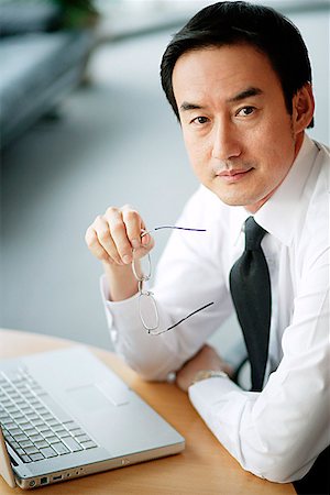 simsearch:694-03330980,k - Businessman looking at camera, laptop open in front of him Stock Photo - Premium Royalty-Free, Code: 656-01768777