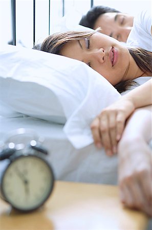 simsearch:656-01768333,k - Couple sleeping on bed, alarm clock in foreground, selective focus Stock Photo - Premium Royalty-Free, Code: 656-01768947