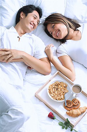 Couple lying on bed, breakfast on tray next to them Stock Photo - Premium Royalty-Free, Code: 656-01768943