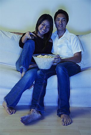 Couple sitting on sofa, watching TV, bowl of popcorn between them Stock Photo - Premium Royalty-Free, Code: 656-01768998