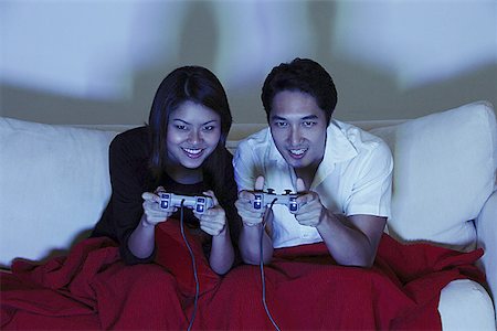 simsearch:656-01770741,k - Couple sitting side by side on sofa, playing with video games Foto de stock - Royalty Free Premium, Número: 656-01769009