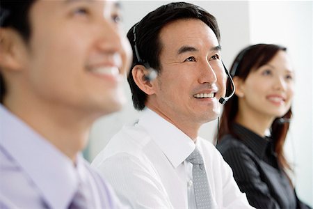 simsearch:628-02954142,k - Executives in a row, wearing headsets, looking away, smiling Fotografie stock - Premium Royalty-Free, Codice: 656-01770030