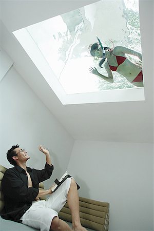 Man in living room, waving at woman in swimming pool through the skylight Stock Photo - Premium Royalty-Free, Code: 656-01770441